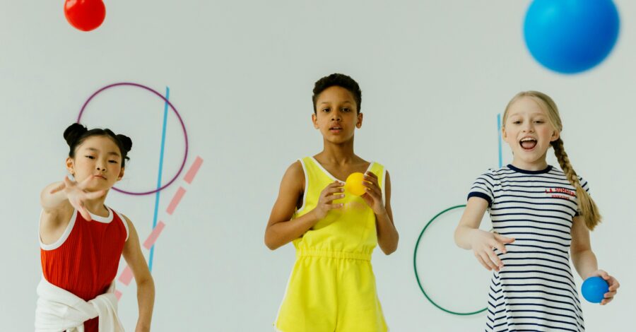 Three young people stand playing with brightly coloured balls and large rings.