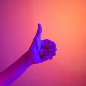 A hand showing a thumbs up lit by a blue light on an orange background.