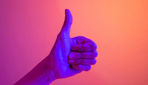 A hand showing a thumbs up lit by a blue light on an orange background.