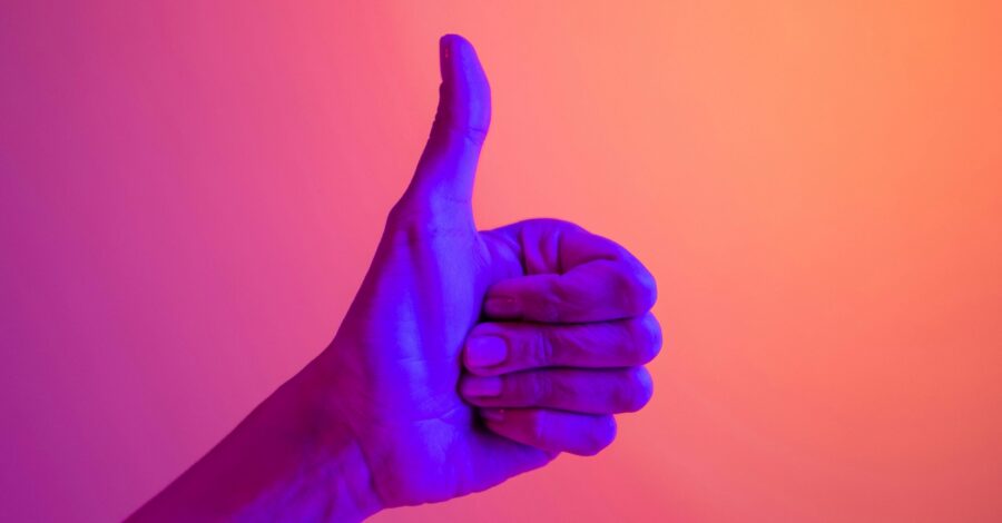 A hand showing a thumbs up lit by a blue light on an orange background.