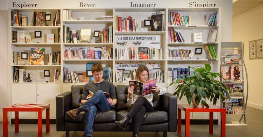 Two people sitting next to one another on a sofa reading.