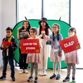 A group of children holding word boards, a microphone and a film action board.