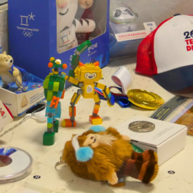 A collection of Olympics memorabilia on a table. There are models of Olympic mascots, a baseball cap and medals.