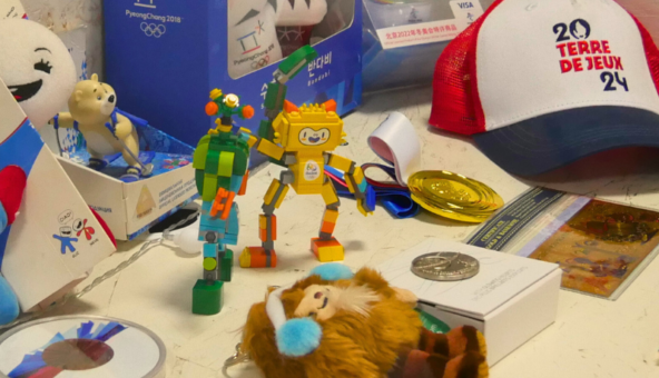A collection of Olympics memorabilia on a table. There are models of Olympic mascots, a baseball cap and medals.