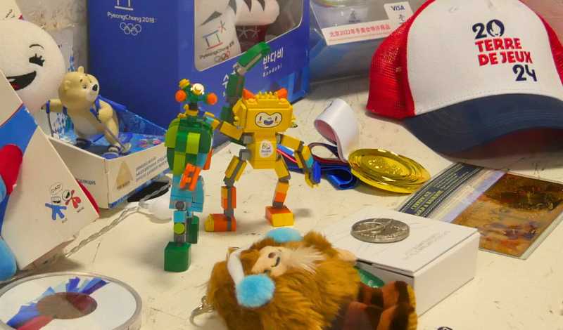 A collection of Olympics memorabilia on a table. There are models of Olympic mascots, a baseball cap and medals.