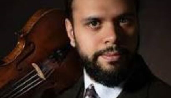 The head and shoulders of violinist and musician Faz Shah. He wears a white shirt, tie and jacket and holds a violin on his shoulder.