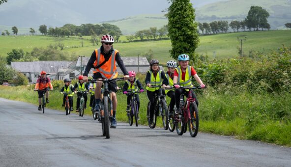 A group of people cycling down a country lane wearing yellow and orange hi-vis vests.