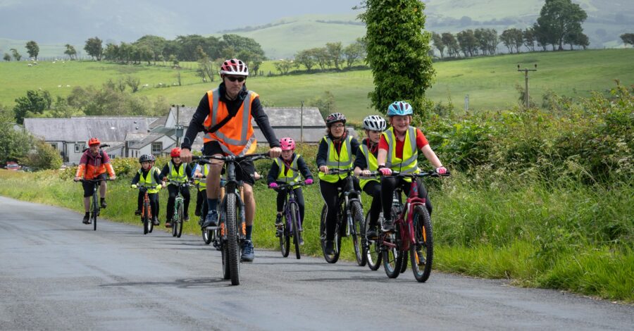 A group of people cycling down a country lane wearing yellow and orange hi-vis vests.