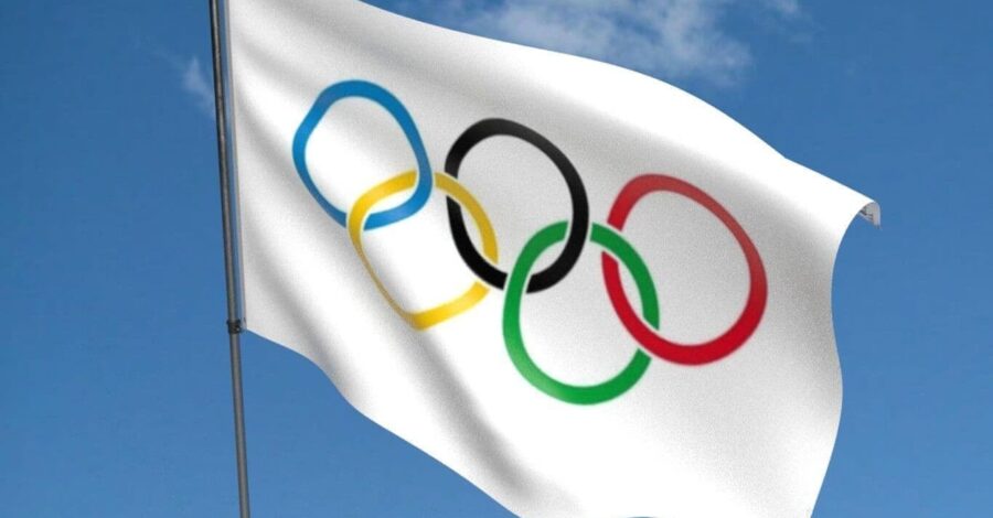 The Olympic flag, consisting of five rings of blue, yellow, black, green and red on a white background, blowing in a breeze under a blue sky.