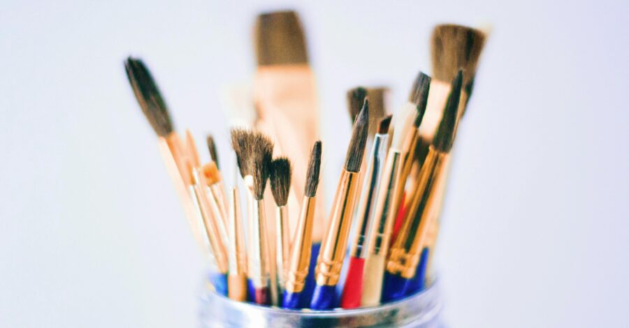 A glass jar with different sized paint brushes in it.