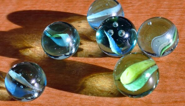 Six glass marbles on top of a wooden table.