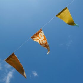 Orange, yellow and red bunting flying in a blue sky during the daytime.