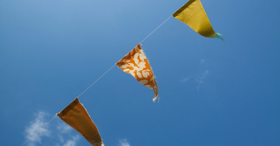 Orange, yellow and red bunting flying in a blue sky during the daytime.