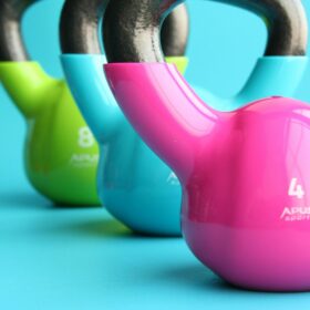 Three kettlebells, coloured pink, blue and green, placed in a line on a blue floor.