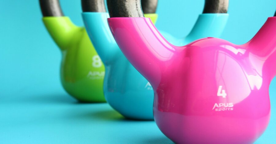 Three kettlebells, coloured pink, blue and green, placed in a line on a blue floor.