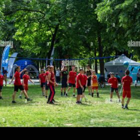 A group of people playing sports in a park. They are wearing red and black sports kits.