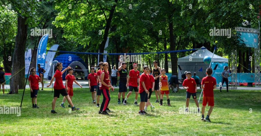 A group of people playing sports in a park. They are wearing red and black sports kits.