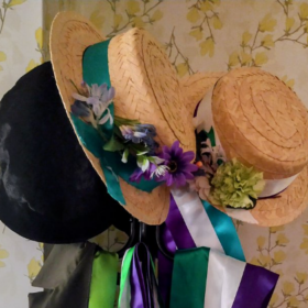 A couple of straw summer hats, decorated with flowers and ribbons, hanging on coat hooks