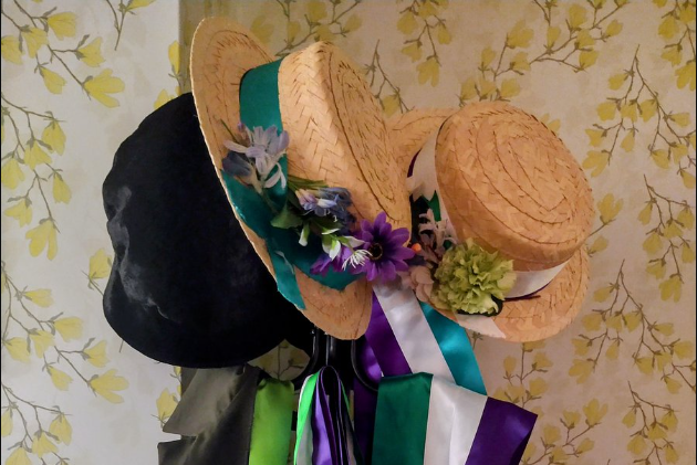 A couple of straw summer hats, decorated with flowers and ribbons, hanging on coat hooks