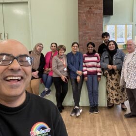 A group of people of different ages standing inside Crumpsall Community Hall. They are smiling.