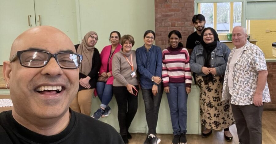 A group of people of different ages standing inside Crumpsall Community Hall. They are smiling.