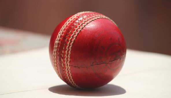 Close up of a red leather cricket ball on a hard surface.