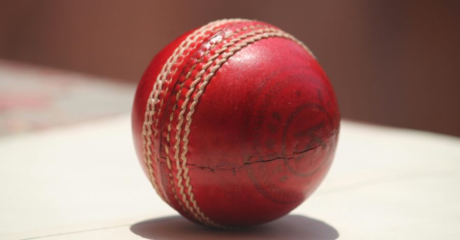 Close up of a red leather cricket ball on a hard surface.