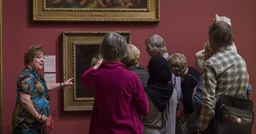 A group of people looking at framed artwork on the walls of a gallery.