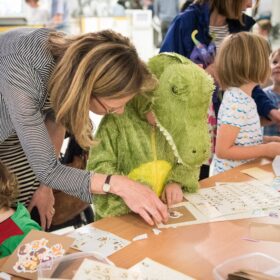 Child in a crocodile costume doing a craft activity with a woman and other children