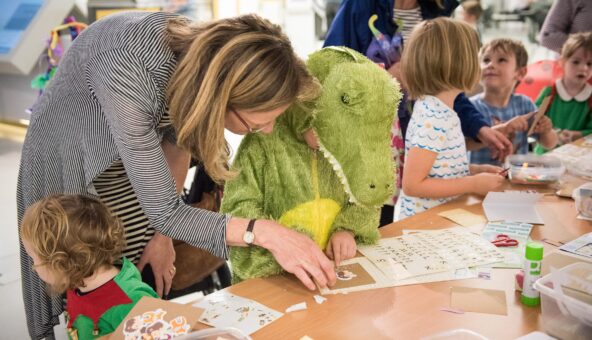 Child in a crocodile costume doing a craft activity with a woman and other children