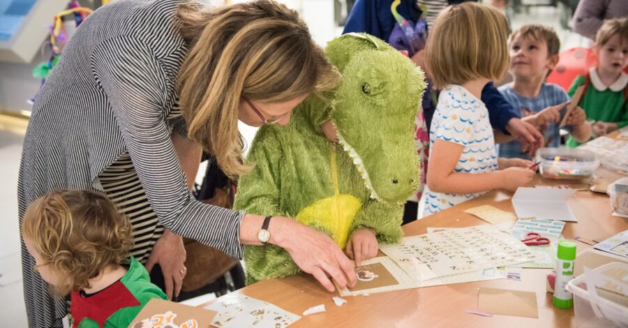 Child in a crocodile costume doing a craft activity with a woman and other children