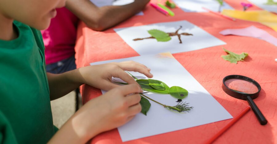 A child using leaves and collage to create a bird on a piece of white paper.