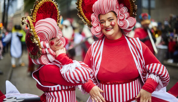 Two people in red and white fancy dress and wigs taking part in the Manchester Christmas Parade.