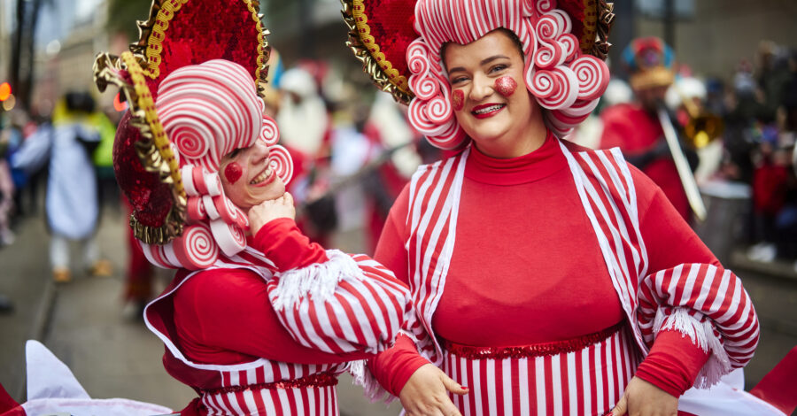 Two people in red and white fancy dress and wigs taking part in the Manchester Christmas Parade.