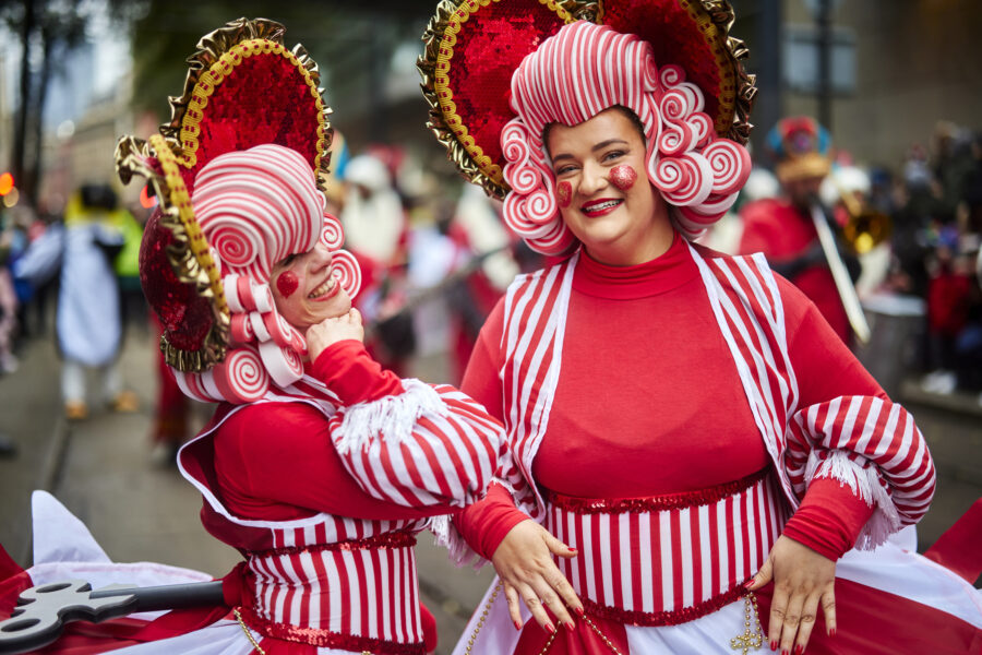 Two people in red and white fancy dress and wigs taking part in the Manchester Christmas Parade.