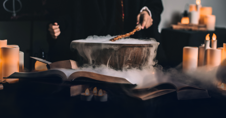 A cauldron bubbling with steam on a table top as somebody stirs it. The cauldron is surrounded by candles.