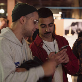 Two adults stand close together looking at a mobile phone.