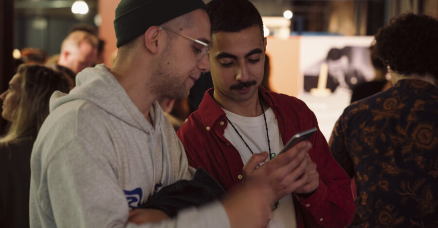 Two adults stand close together looking at a mobile phone.