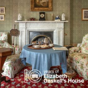 The fireplace and a table with a blue tablecloth on it in the drawing room of Elizabeth Gaskell's House. At the bottom of the image is the text ' 10 years of Elizabeth Gaskell's House'.