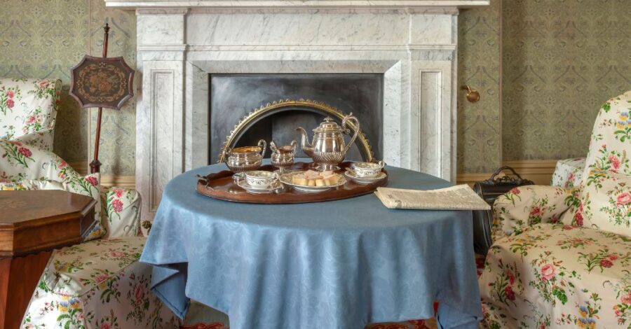 The fireplace and a table with a blue tablecloth on it in the drawing room of Elizabeth Gaskell's House. At the bottom of the image is the text ' 10 years of Elizabeth Gaskell's House'.