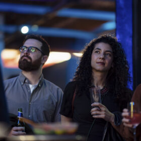 Two adults stand next to oneanother, each holding a drink.