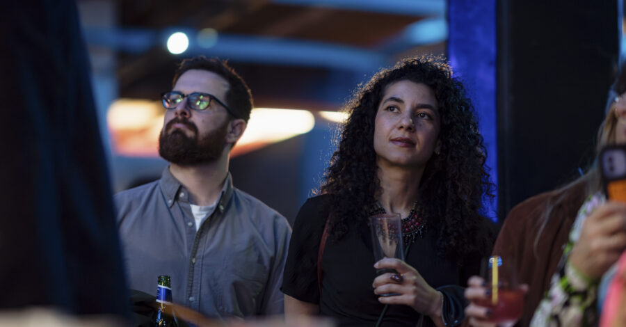 Two adults stand next to oneanother, each holding a drink.