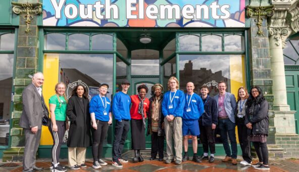 The people who work at Youth Elements standing infront of their headquarters with a sign above that reads 'Youth Elements'.