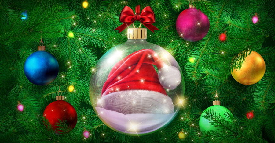 A giant glass bauble with a red and white Santa hat inside hanging from a Christmas tree.