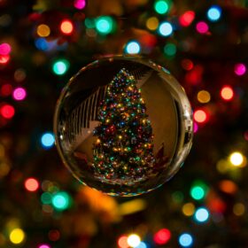 Close up of a bauble showing the reflection of a lit up Christmas tree. Colourful Christmas lights in the background.
