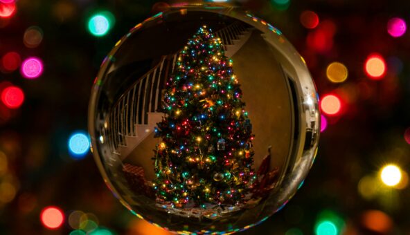 Close up of a bauble showing the reflection of a lit up Christmas tree. Colourful Christmas lights in the background.