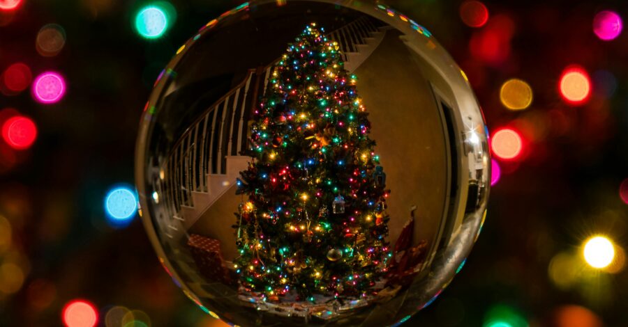 Close up of a bauble showing the reflection of a lit up Christmas tree. Colourful Christmas lights in the background.