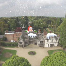 The exterior of Wythenshawe Hall on a snowy day, with snow on the rooftops and snow falling from the sky.