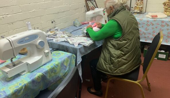 A woman sittng down on a chair at a table using a sewing machine