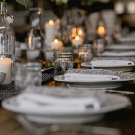 A table set for a dinner party with white plates, cutlery and glass jars.